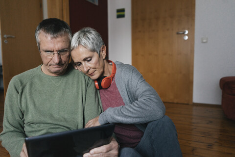 Älteres Paar sitzt zu Hause auf dem Boden und schaut auf ein Tablet, lizenzfreies Stockfoto