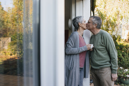 Affectionate senior couple kissing at terrace door - KNSF05567