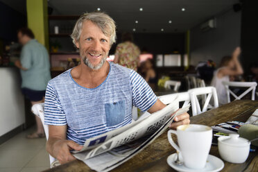 Porträt eines lächelnden reifen Mannes, der in einem Café sitzt und Zeitung liest - ECPF00515