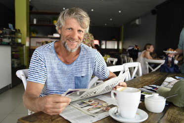 Porträt eines lächelnden reifen Mannes, der in einem Café sitzt und Zeitung liest - ECPF00516