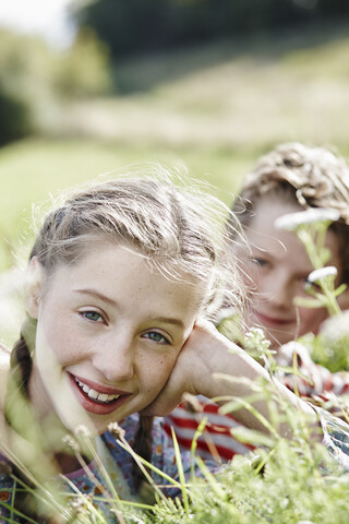 Porträt eines lächelnden Mädchens auf einer Wiese liegend mit kleinem Bruder im Hintergrund, lizenzfreies Stockfoto