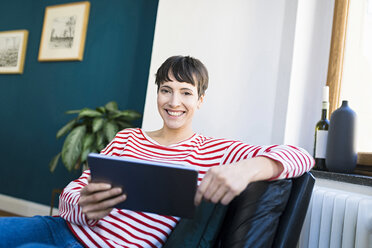 Portrait of happy short-haired woman in lounge chair holding tablet - SBOF01731