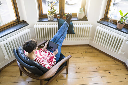 Short-haired woman relaxing in lounge chair holding tablet in stylish apartment - SBOF01732