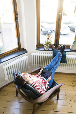 Short-haired woman relaxing in lounge chair holding tablet in stylish apartment stock photo