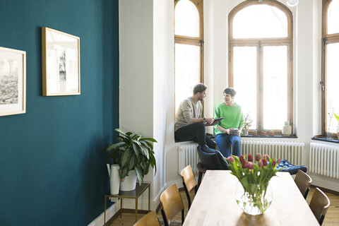 Lässiges Paar, das sich unterhält und am Fenster einer stilvollen Wohnung sitzt, lizenzfreies Stockfoto