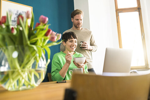 Glückliches Paar mit Blick auf den Laptop im Heimbüro - SBOF01743