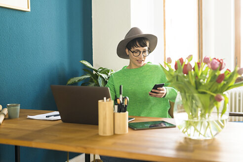 Geschäftsfrau im Heimbüro, die an ihrem Laptop arbeitet und auf ihr Telefon schaut - SBOF01747