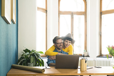 Lässiges Unternehmerpaar im Heimbüro, das am Laptop arbeitet und sich umarmt - SBOF01751