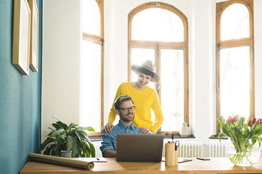 Lässiges Unternehmerpaar im Heimbüro, das am Laptop arbeitet und lächelt - SBOF01752