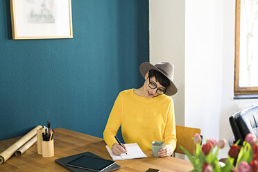 Geschäftsfrau im Büro zu Hause, die auf einem Stück Papier schreibt und eine Kaffeetasse hält - SBOF01753