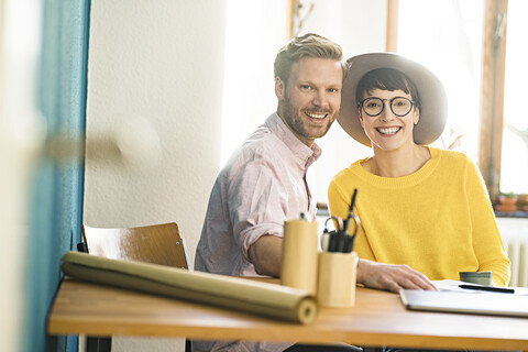 Porträt des glücklichen Paares am Holztisch in ihrem Heimbüro, lizenzfreies Stockfoto