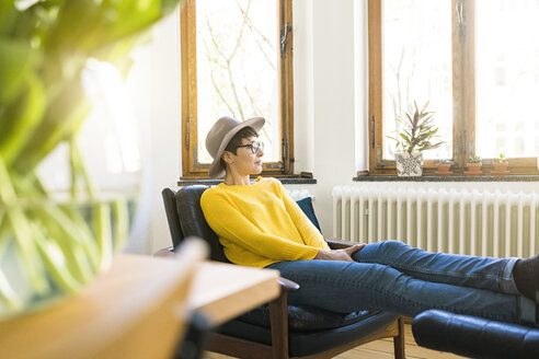 Nachdenkliche Frau entspannt sich in einem Sessel in einer stilvollen Wohnung und schaut aus dem Fenster - SBOF01766