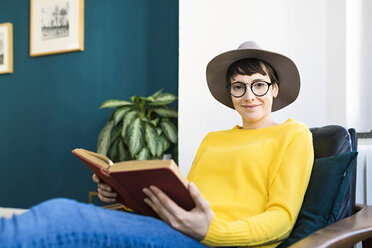 Portrait of smiling woman relaxing in lounge chair reading a book - SBOF01768