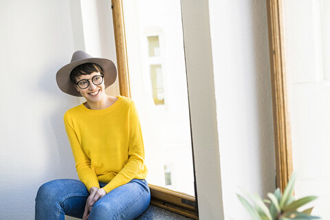 Glückliche Frau sitzt auf der Fensterbank und schaut nach draußen, lizenzfreies Stockfoto