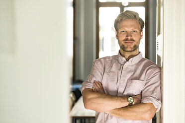 Portrait of confident casual man leaning against door case at home - SBOF01777