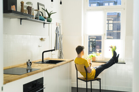 Man relaxing on chair with his feet on the windowsill in his kitchen looking outside stock photo