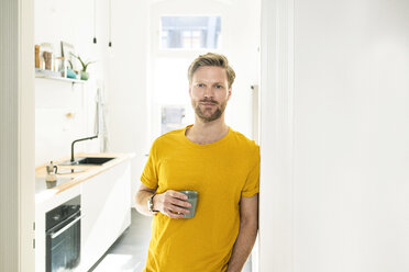 Selbstbewusster, lässiger Mann mit Kaffeetasse, der sich gegen ein Türgehäuse lehnt - SBOF01784