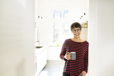 Selbstbewusste kurzhaarige Frau mit Kaffeetasse, die sich gegen eine Tür lehnt - SBOF01786