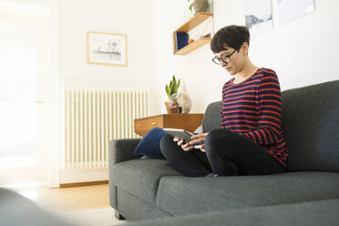 Lässige kurzhaarige Frau, die sich in einem modernen Wohnzimmer auf einer Couch entspannt und ein Tablet benutzt - SBOF01792