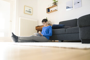 Casual short-haired woman relaxing in modern living room using a tablet - SBOF01793