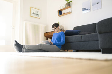 Lässige kurzhaarige Frau entspannt sich in einem modernen Wohnzimmer und benutzt ein Tablet - SBOF01793