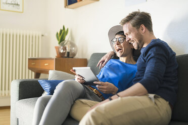 Happy casual couple relaxing on couch using tablet and laughing - SBOF01796