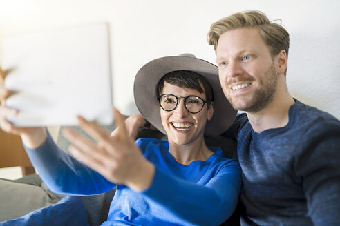 Glückliches lässiges Paar macht ein Selfie mit Tablet im Wohnzimmer - SBOF01797