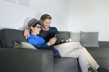 Happy casual couple relaxing on couch using tablet - SBOF01798