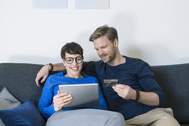 Happy casual couple relaxing on couch using tablet and holding credit card - SBOF01799