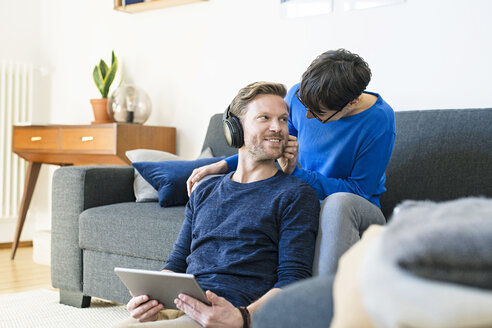 Lässiges Paar mit Kopfhörern, das sich auf der Lounge-Couch in seinem modernen Wohnzimmer entspannt - SBOF01800