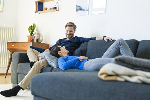 Glückliches Paar entspannt sich auf der Couch in ihrem modernen Wohnzimmer - SBOF01801