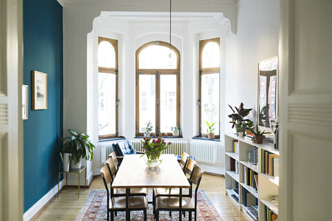 Holztisch und Stühle im modernen Wohnzimmer mit großer Fensterfront in einer stilvollen Wohnung, lizenzfreies Stockfoto