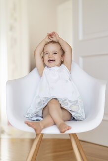 Porträt eines lachenden Kleinkindes, das mit erhobenen Armen auf einem Stuhl sitzt - DIGF05857