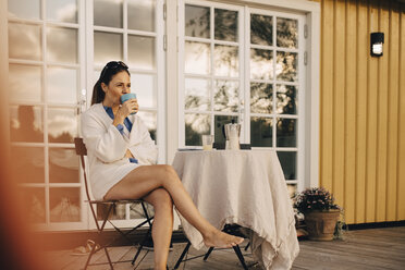 Full length of mature woman drinking coffee while sitting at patio in holiday villa - MASF11072