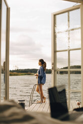 Frau in voller Länge auf der Terrasse am See stehend - MASF11088