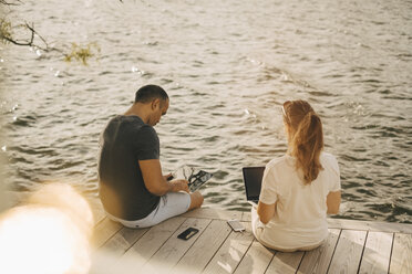 Älteres Paar benutzt Laptop, während es im Sommerurlaub auf der Terrasse am See sitzt - MASF11104