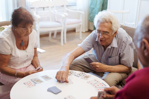 Ältere Menschen spielen Karten am Tisch im Altersheim, lizenzfreies Stockfoto