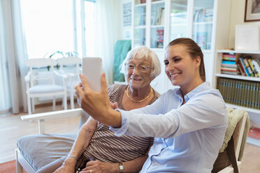 Lächelnde ältere Frau und ihre Enkelin machen ein Selfie mit dem Handy während eines Besuchs im Pflegeheim - MASF11137