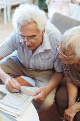 High angle view of senior couple doing crossword puzzle in newspaper at nursing home - MASF11144