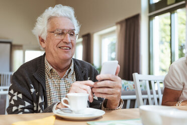 Älterer Mann benutzt Mobiltelefon am Frühstückstisch im Pflegeheim - MASF11147