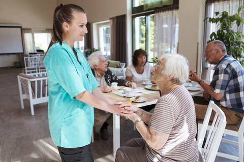 Krankenschwester tröstet ältere Frau beim Frühstück im Pflegeheim, lizenzfreies Stockfoto