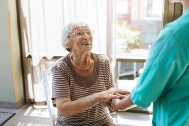 Lächelnde ältere Frau, die die Hände des Pflegepersonals im Pflegeheim hält - MASF11154