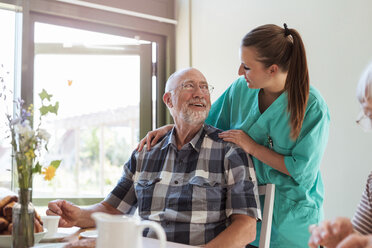 Senior man talking with female nurse while having breakfast in nursing home - MASF11156