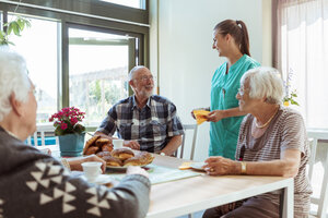 Lächelnder älterer Mann und Krankenschwester unterhalten sich beim Frühstück im Pflegeheim - MASF11158
