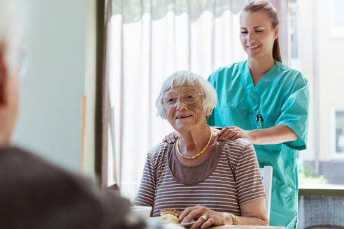 Lächelnde Pflegerin massiert die Schultern einer älteren Frau zu Hause - MASF11159