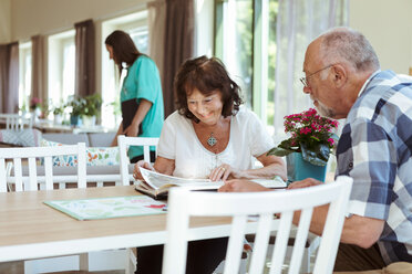 Älteres Paar liest gemeinsam ein Buch am Tisch im Pflegeheim - MASF11172