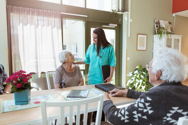 Junge Krankenschwester im Gespräch mit einer älteren Frau, die am Tisch im Pflegeheim sitzt - MASF11177