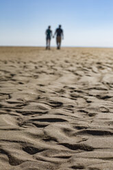 Wave pattern on the beach with silhouette of couple walking hand in hand in the background - JATF01122