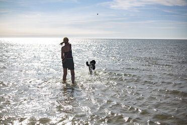Frankreich, Rückenansicht einer Frau, die ihrem Hund am Meer einen Ball zuwirft - JATF01125
