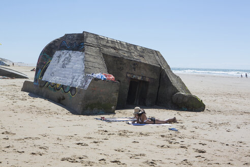 Frankreich, Gironde, Frau liegt am Strand vor einem Bunker aus dem Zweiten Weltkrieg und liest ein Buch - JATF01129